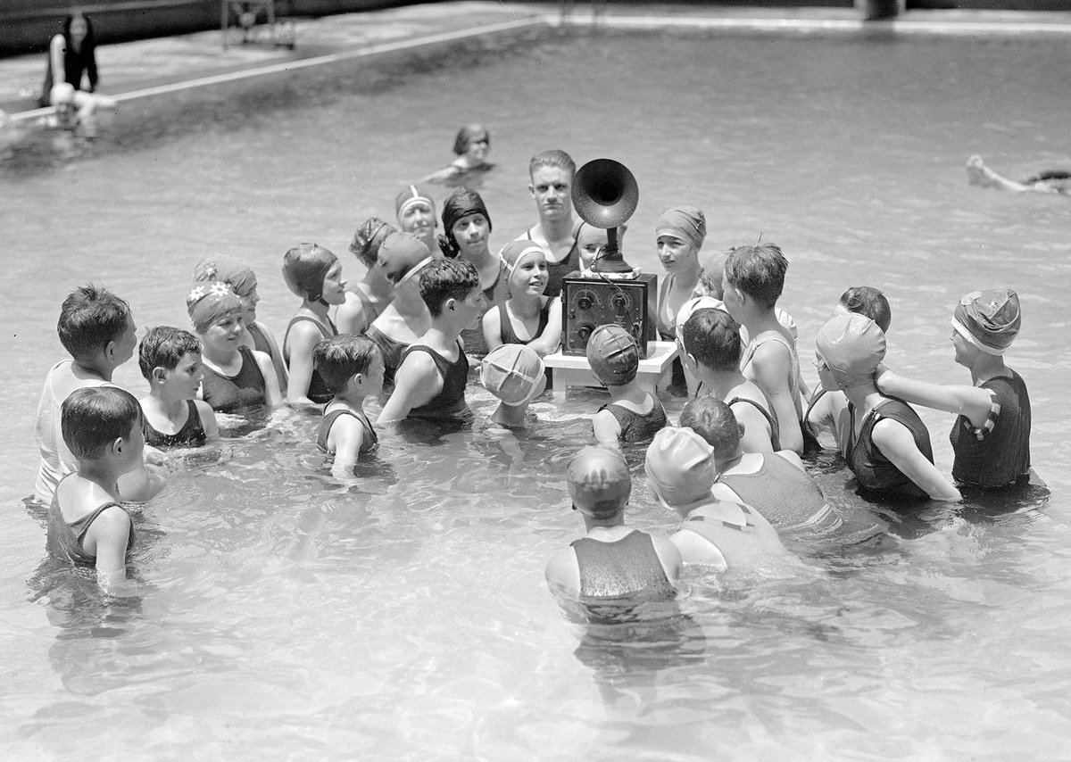 Children listen to a battery-powered radio receiver that is set on a table in a swimming pool in Washington, D.C., in July of 1924.